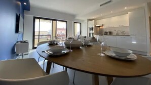 A modern dining area with a round table set for four, a kitchen in the background, and large windows offering a view.