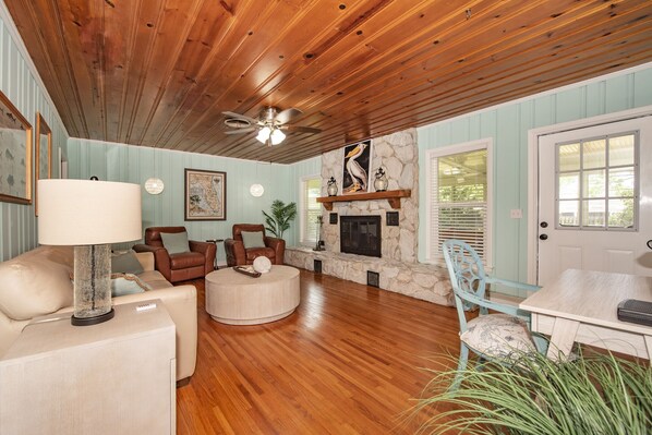 A cozy living room with wooden floors, a stone fireplace, and a ceiling fan. - Short term stay coastal furnished w/ utilities in Clearwater Florida near Beach. (Clearwater)