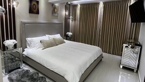 Une chambre à coucher moderne avec un grand lit, un miroir, une table de chevet et un téléviseur.