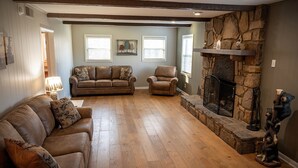 Una sala de estar acogedora con chimenea de piedra, piso de madera y dos sofás de cuero.