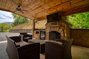 An outdoor patio with wicker furniture, a stone fireplace, and a stone oven. - 4,900 sq ft, 5 bedroom, large game room, and hot tub next to Rocky Top Sports.  (Gatlinburg)