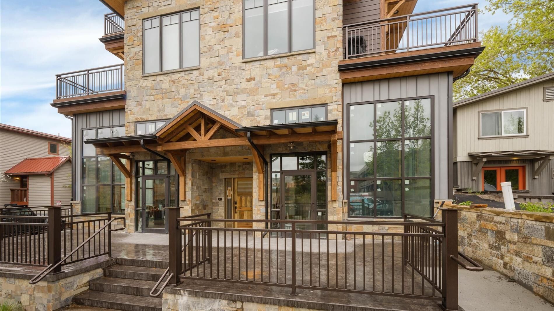 A multi-story stone building with large windows, a covered entrance, and a metal fence.