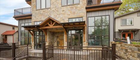 A multi-story stone building with large windows, a covered entrance, and a metal fence.