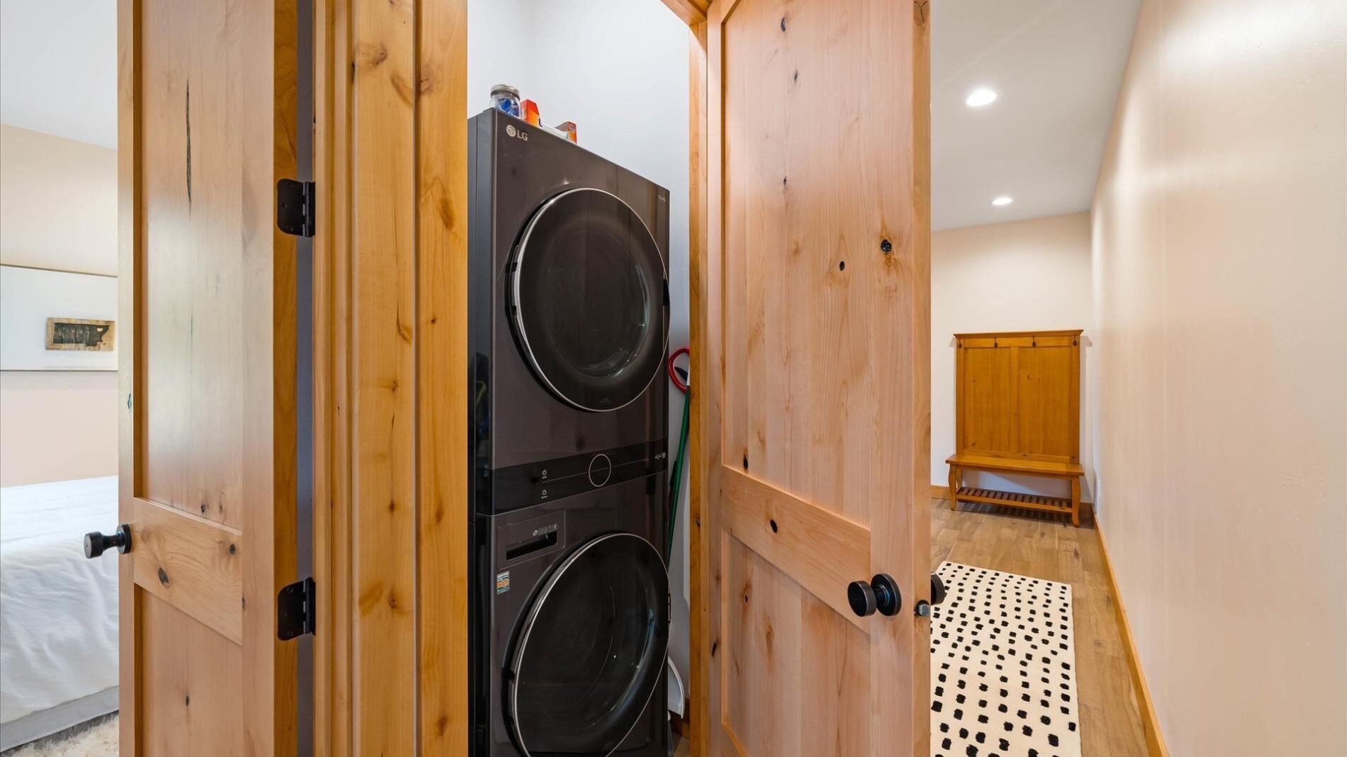 Un espace buanderie comprenant deux machines à laver superposées, des portes en bois, un banc et un tapis à pois.
