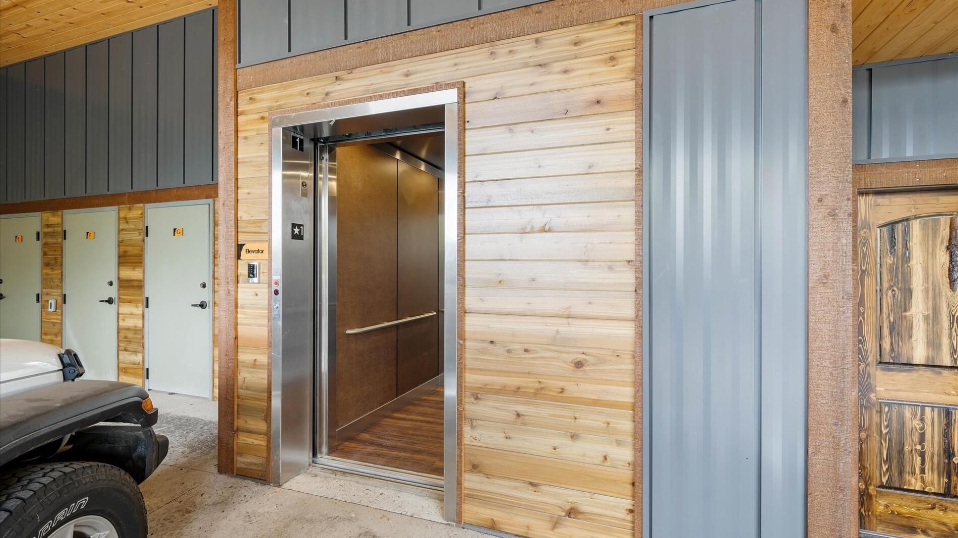 A modern elevator with a metallic interior, adjacent to a wooden wall with a metal panel.