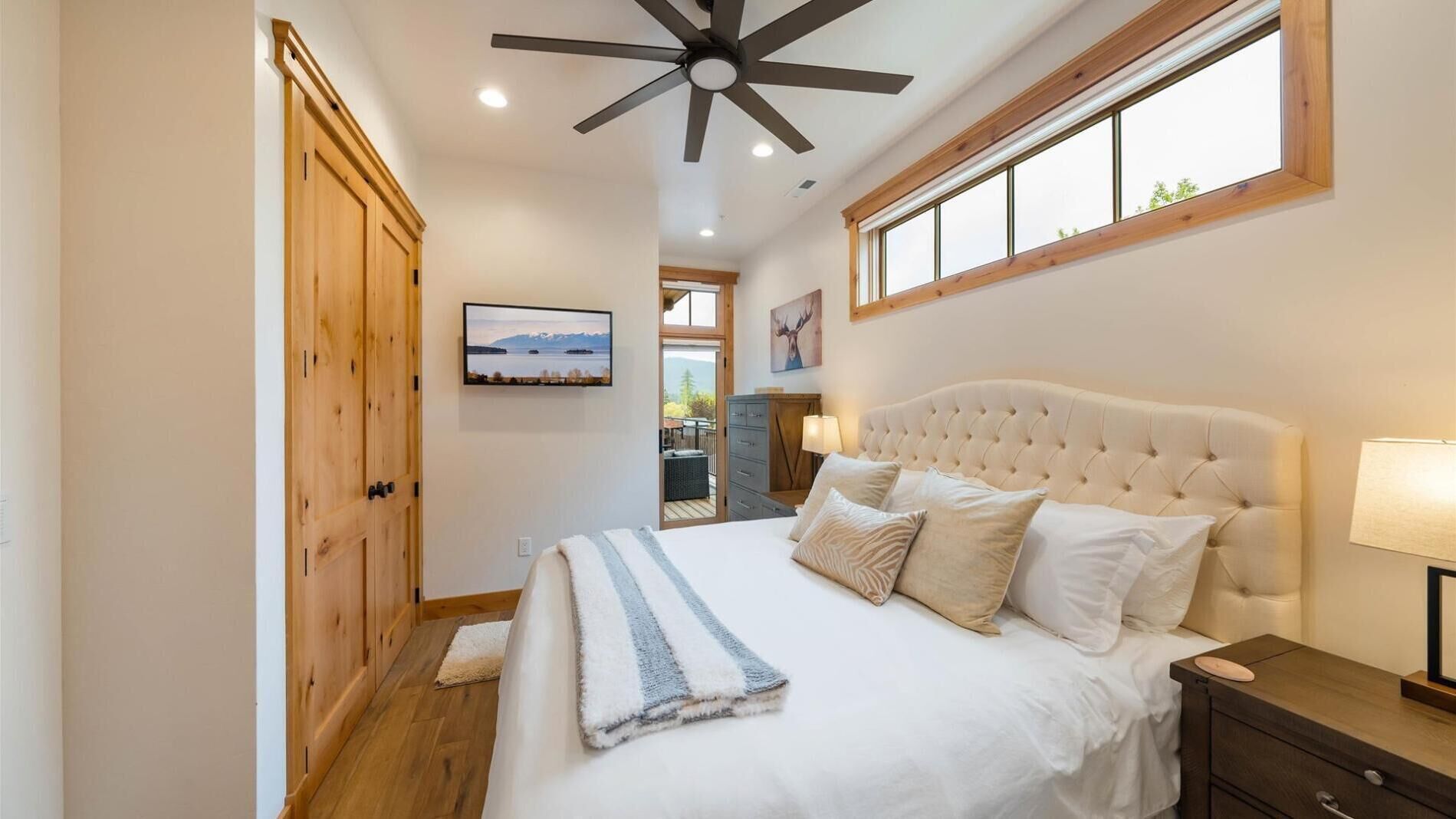 A bedroom with a large bed, a ceiling fan, a window with a view, and wooden doors.