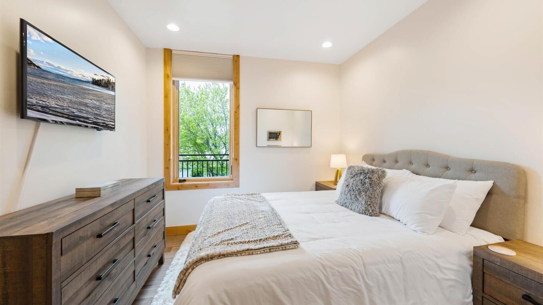Un dormitorio con cama, cómoda, ventana con vista a árboles y un cuadro en la pared.