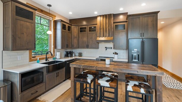 A modern kitchen with dark wooden cabinets, a large island with bar stools, a built-in oven, and a refrigerator. - New Listing/Brand New Construction in the Heart of Downtown Whitefish (Whitefish)