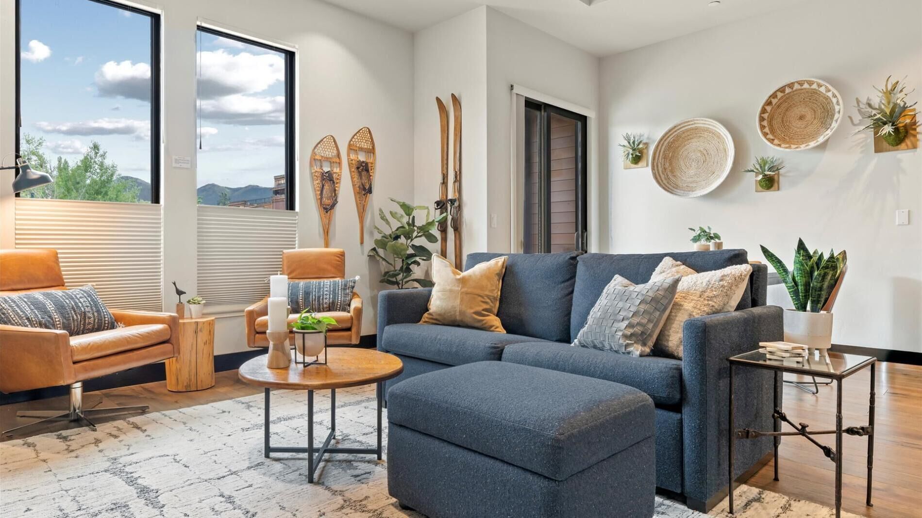 A modern living room with a blue sofa, a wooden coffee table, and a leather armchair. There are decorative plates on the wall and a plant on the side table.