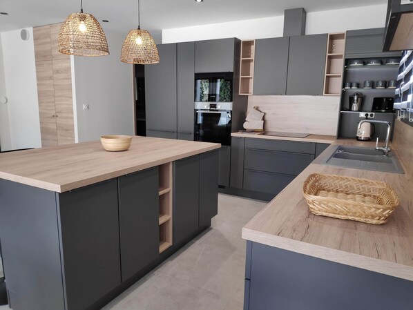 Uma cozinha moderna com armários escuros, uma ilha de madeira e iluminação pendente.