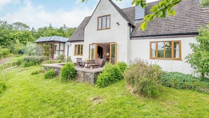 Une maison à deux étages avec des fondations en pierre, un grand patio ouvert aménagé avec du mobilier d’extérieur et un jardin.