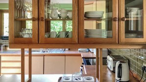 Une cuisine avec des meubles en bois contenant de la vaisselle et des verres, un évier, un grille-pain et une fenêtre donnant sur un paysage verdoyant.