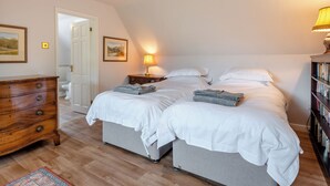 Une chambre avec deux lits, une commode en bois, une table de chevet avec une lampe et une bibliothèque.