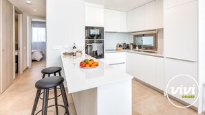 A modern kitchen with white cabinetry, a central island with stools, and a dining area. - Blue View | sea view - garden - pool (Mijas Costa)