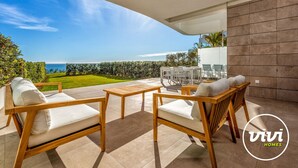 A modern outdoor patio with wooden furniture, a view of the sea, and a well-maintained lawn. - Blue View | sea view - garden - pool (Mijas Costa)