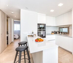 Una cocina moderna con muebles blancos, una isla central con taburetes y un comedor.