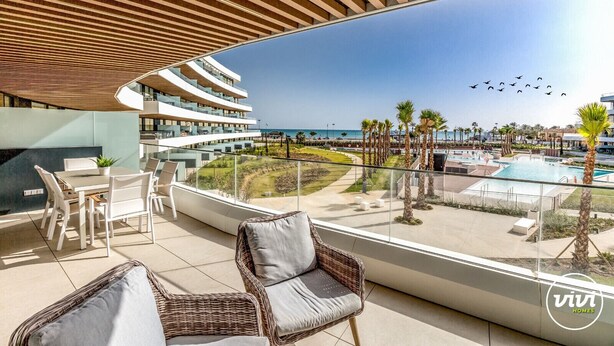 Ein moderner Hotelbalkon mit Pool, Liegestühlen und Blick auf Strand und Meer.