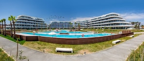 A modern hotel with a central swimming pool, surrounded by palm trees and a multi-story building in the background. - ViVi Homes 2, Rembrandt apartment (Torremolinos)
