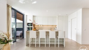 Eine moderne Küche mit weißen Schränken, einer zentralen Kochinsel mit Barhocker und einer Glastür zum Balkon.