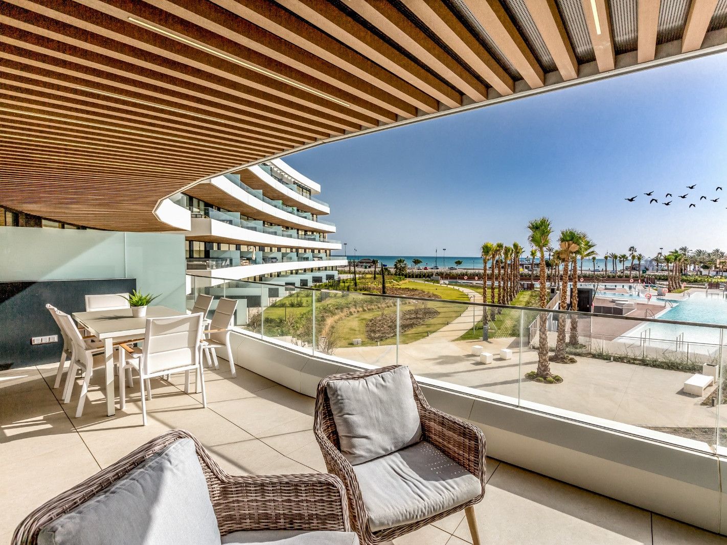 Un balcon moderne d’hôtel avec une piscine, des chaises longues et une vue sur la plage et l’océan.
