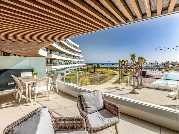 Ein moderner Hotelbalkon mit Pool, Liegestühlen und Blick auf Strand und Meer.