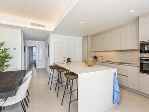A modern kitchen with a central island, bar stools, a coffee machine, and built-in appliances. - Fari | Beach - terrace - pool (Torremolinos)