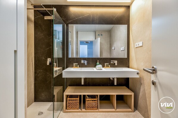 Une salle de bain moderne avec une douche à parois de verre, un lavabo blanc avec un miroir au-dessus et un banc en bois en dessous.