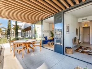 A modern living area with a wooden ceiling, a glass door leading to a balcony, and a dining set.