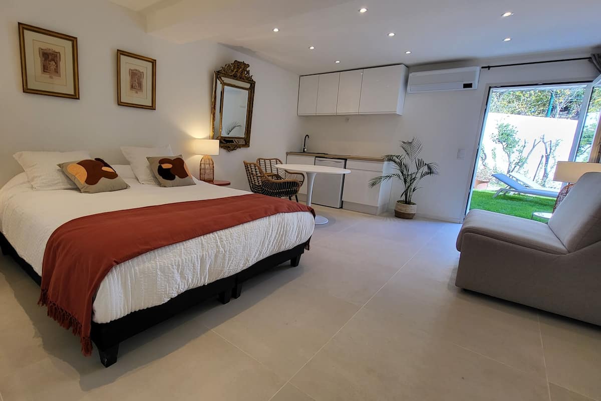 A modern bedroom with a large bed, a small desk, a chair, and a view of the garden.