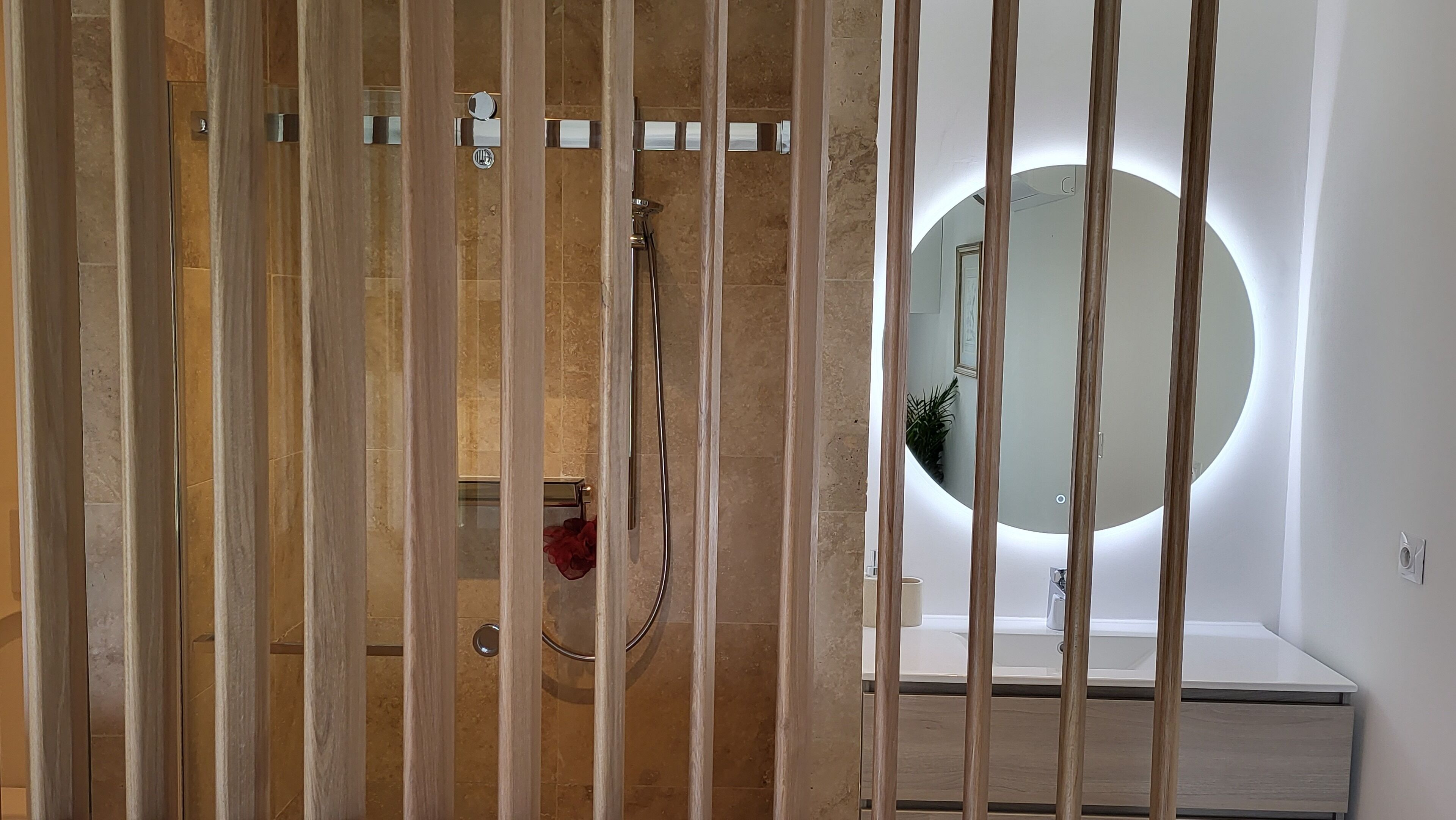 Een moderne badkamer met een douchecabine van hout, een ronde spiegel en een witte wastafel.