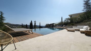 Relax by the infinity pool surrounded by lush greenery and a stone wall, with comfortable seating options available.