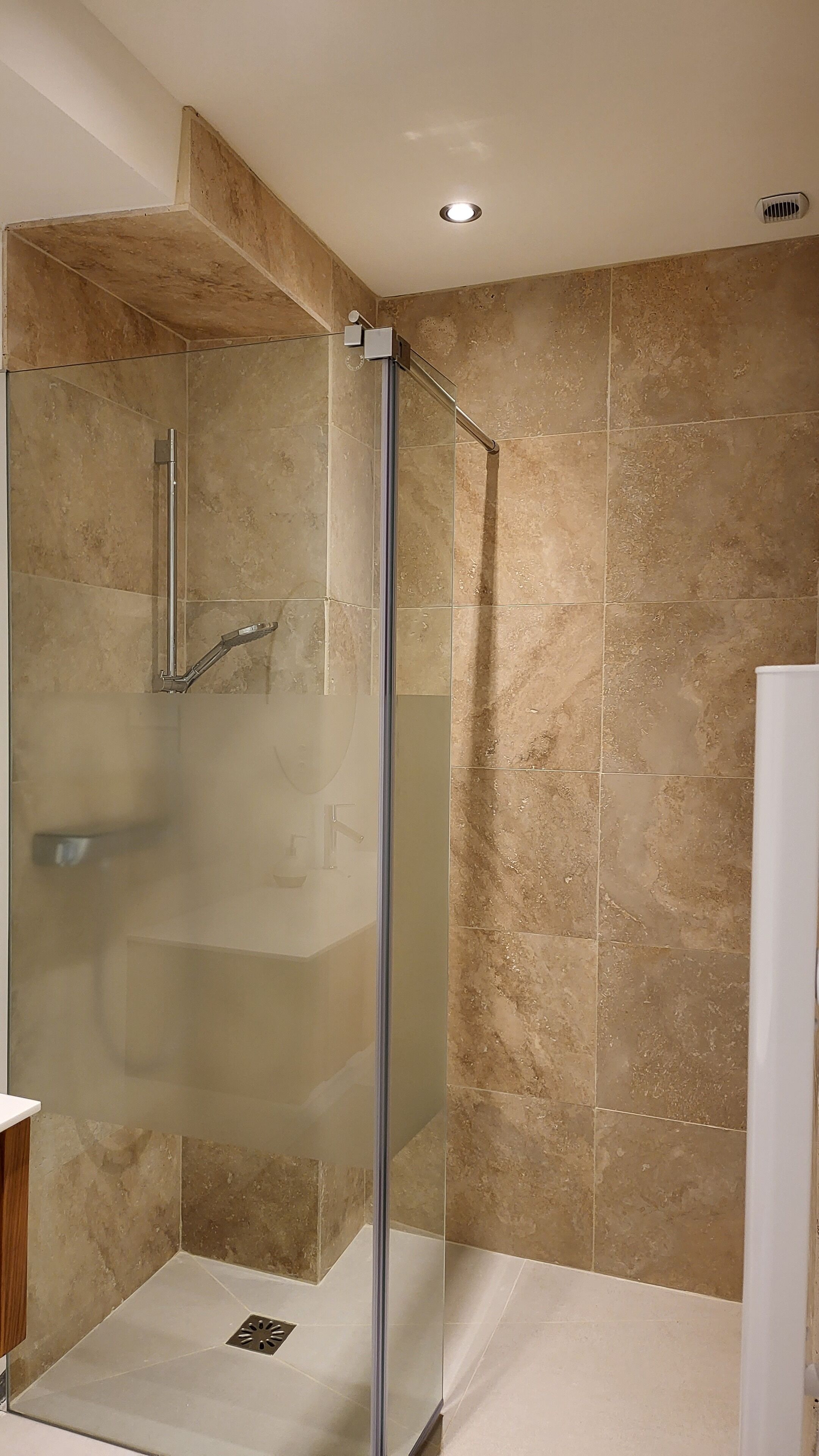 A glass-enclosed shower with a vertical handle and a glass door.