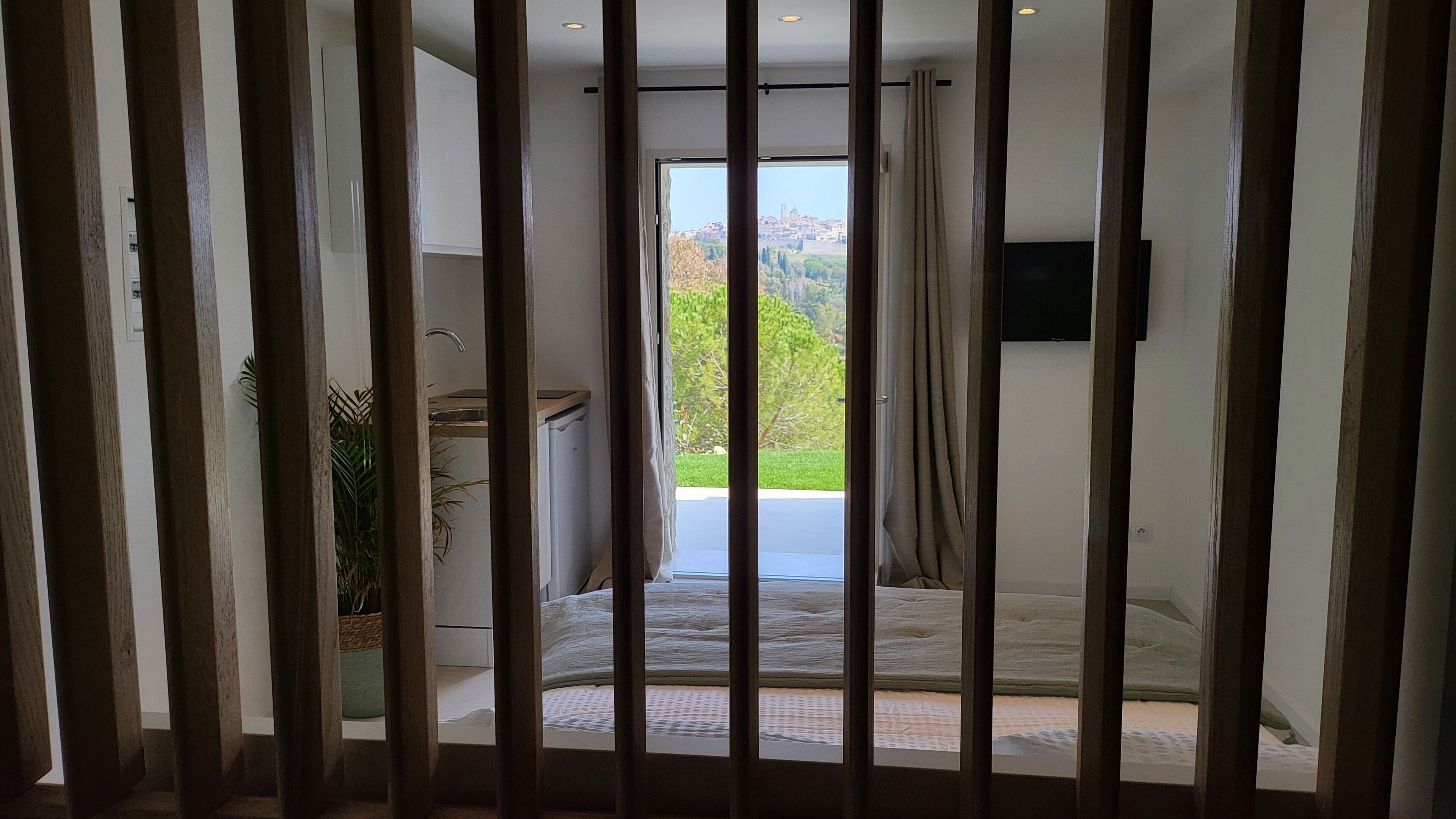 Une chambre à coucher avec un lit, un téléviseur fixé au mur et une vue sur l’extérieur par une fenêtre.