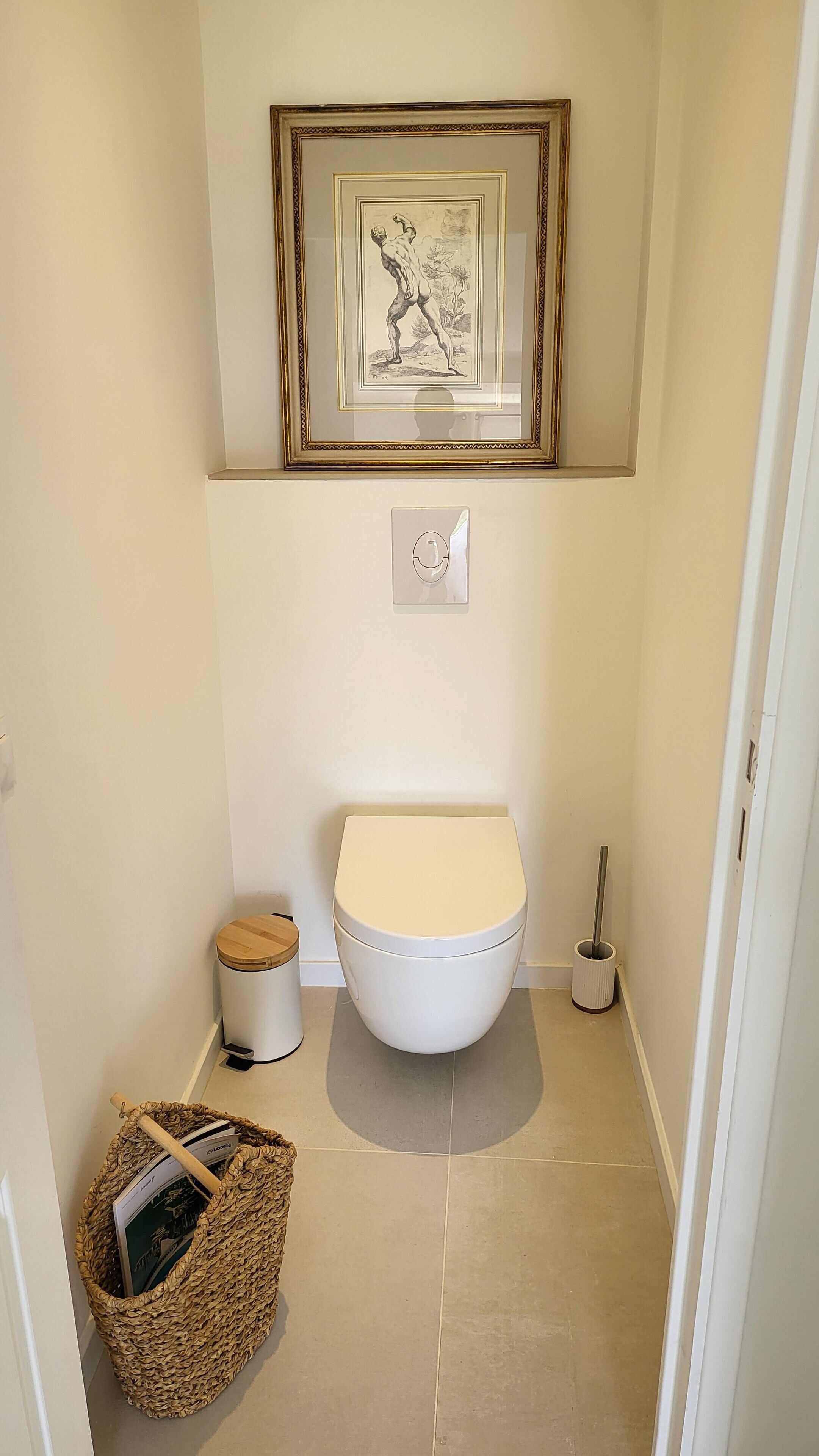 A small, clean bathroom with a toilet, a trash bin, and a broom.