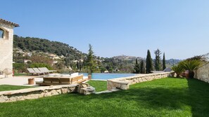 A pool area with stone walls and a view of a hillside village. - Ideal BnB (Saint-Paul-de-Vence)