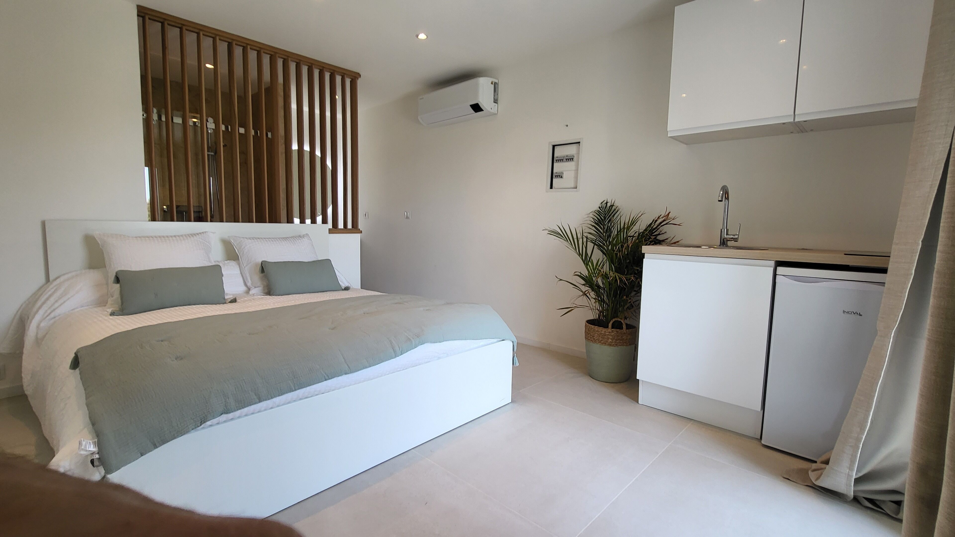 A bedroom with a bed, a bedside table, a potted plant, a wardrobe, and a built-in air conditioning unit.
