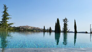 Una piscina cristalina con reflejos de árboles altos y una colina distante con edificios.
