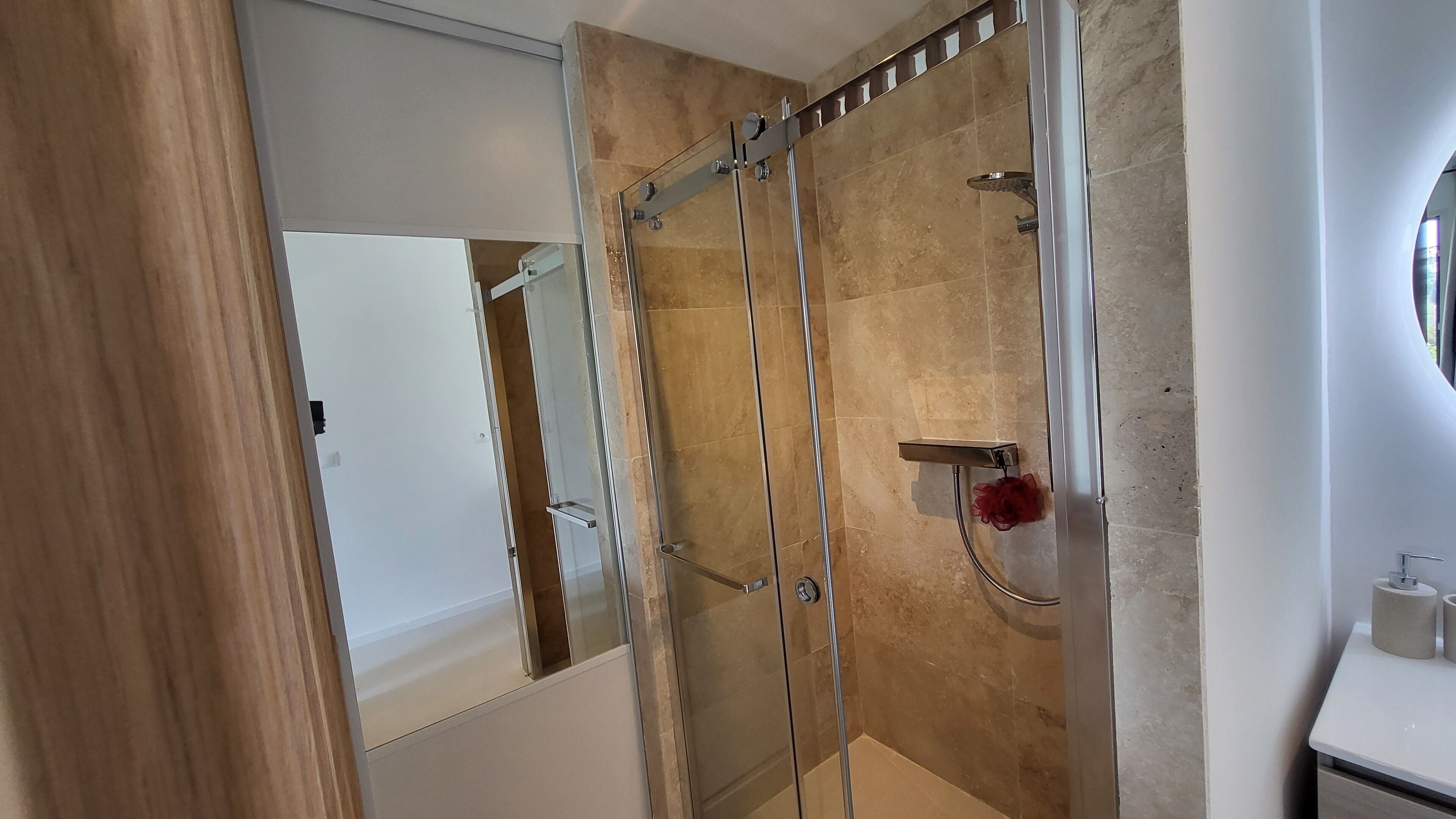 A modern bathroom with a glass-enclosed shower, a white sink, and a mirror.