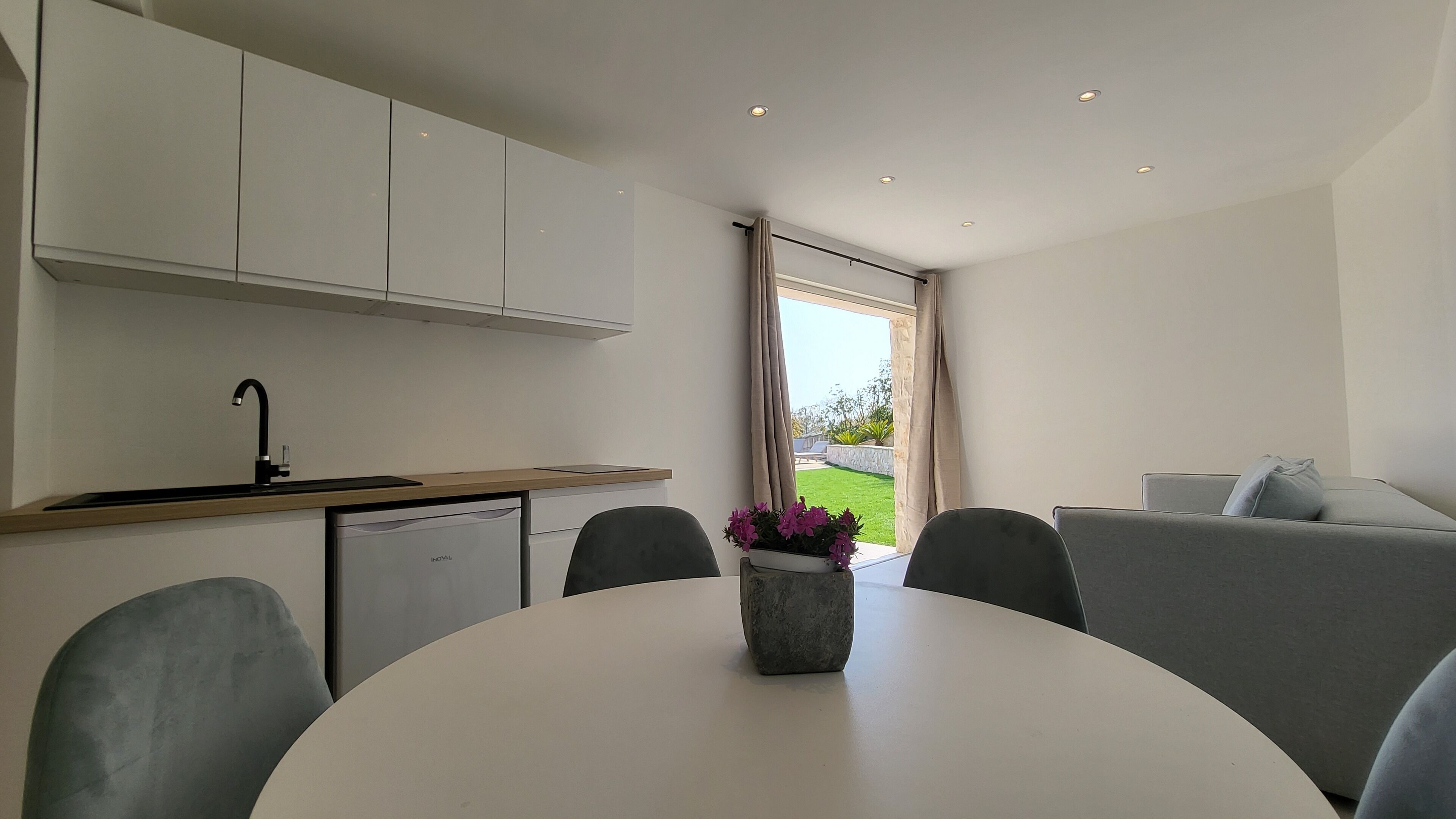 Una cocina moderna con armarios blancos, lavavajillas integrado y un comedor con mesa y sillas redondas.