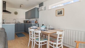 A compact kitchen with blue cabinets, a wooden dining table, and a window above the sink. - Calon Y Mor - Close to Village and Beach (Saundersfoot)