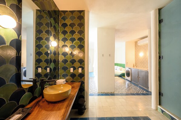 Une salle de bain avec un grand miroir, un lavabo avec un receveur et un mur décoré d’un motif.