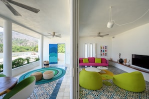 A modern living room with a sofa, green poufs, and a TV. - Casa Dos Aguas: Yelapa Beachfront 1BR with Bay Views & Open-Air Terrace (Yelapa)