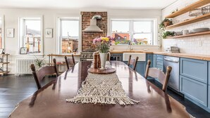 A modern kitchen with a brick wall, wooden cabinets, and a large dining table with a macrame runner.