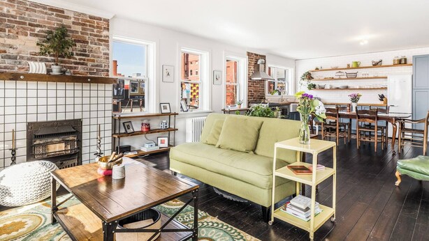 A modern living room with a fireplace, a green sofa, a wooden coffee table, and a dining area with a wooden table and chairs.