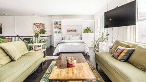 A modern living room with a large bed, green sofas, a wooden coffee table, and a TV mounted on the wall.