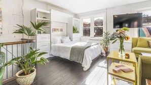 A modern bedroom with a bed, bedside tables, a TV, and a balcony with plants.