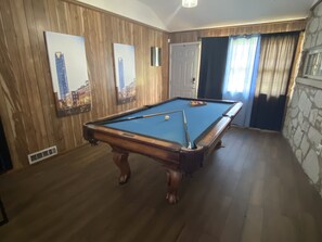 A pool table in a room with wooden paneling, a door, and a stone wall.