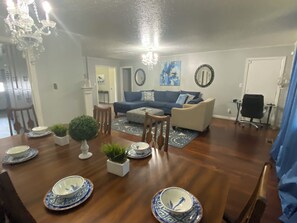 A dining area with a wooden table set for four, surrounded by chairs. There is a blue sofa and a small round table in the background. - A Point of Blue 🔵 Hottub/ Pool table/10 min all OKC (Oklahoma City)