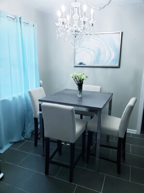 Een eetruimte met een donker houten tafel, zes stoelen, een kroonluchter, een vaas met bloemen en een schilderij aan de muur.