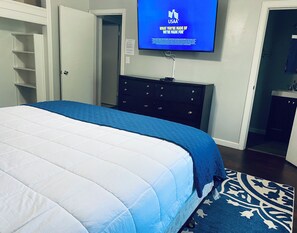A bedroom with a bed, a dresser, a television on the wall, and a door leading to another room. - A Point of Blue 🔵 Hottub/ Pool table/10 min all OKC (Oklahoma City)